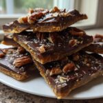 A stack of homemade graham cracker toffee squares topped with melted chocolate, pecans, and sea salt.