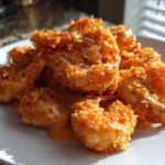 A pile of golden brown, crispy air fryer bang bang shrimp drizzled with a creamy orange sauce on a white plate.