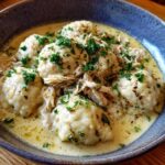Close-up of a bowl of amazing chicken and dumpling, featuring fluffy dumplings in a rich sauce topped with shredded chicken and parsley.