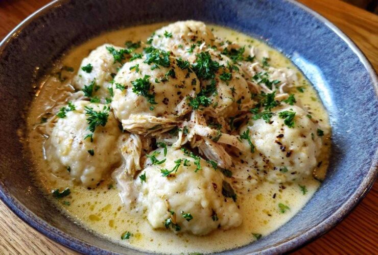 Close-up of a bowl of amazing chicken and dumpling, featuring fluffy dumplings in a rich sauce topped with shredded chicken and parsley.