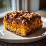 Close-up of a moist slice of pumpkin crunch cake featuring a bright orange layer and a dark, sugary pecan streusel topping.