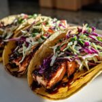 Close-up of three delicious salmon tacos filled with glazed salmon and topped with vibrant purple and green coleslaw.