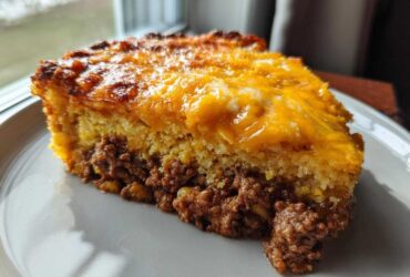 A hearty slice of tamale pie showing a layer of seasoned ground meat topped with golden cornbread and melted cheddar cheese.