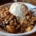 Close-up of a warm serving of apple crisp topped with a melting scoop of vanilla ice cream.
