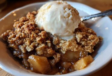 Close-up of a warm serving of apple crisp topped with a melting scoop of vanilla ice cream.