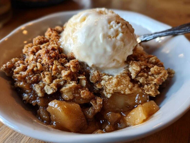 Close-up of a warm serving of apple crisp topped with a melting scoop of vanilla ice cream.