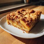 Close-up of a square serving of apple pie bars with a thick, crumbly topping on a white plate.
