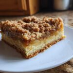 A single serving of rich, layered apple pie bars with a thick crumble topping on a white plate.
