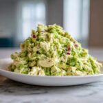 A generous mound of creamy avocado chicken salad mixed with chunks of chicken and red onion served on a white plate.