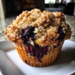 Close-up of a freshly baked blueberry muffin featuring a generous, golden crumb topping and bursting blueberries.