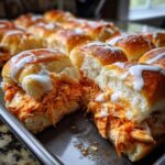 A close-up view of two halves of a buffalo chicken sliders sandwich, showing shredded orange chicken filling and a white ranch or blue cheese drizzle.