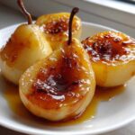 Four glistening baked pears drizzled with caramelized syrup, presented on a white plate.