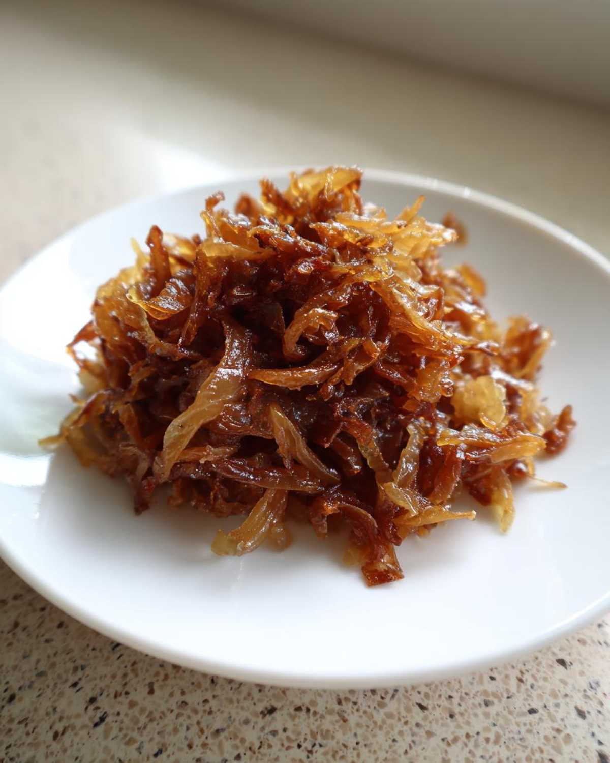A close-up of a small mound of rich, dark brown caramelized onions served on a white saucer.