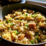 Close-up view of vibrant cauliflower fried rice with scrambled egg and green onions in a dark wok.