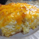 Close-up of a square serving of cheesy potato casserole topped with melted, golden cheddar cheese.