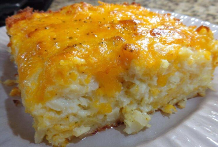 Close-up of a square serving of cheesy potato casserole topped with melted, golden cheddar cheese.