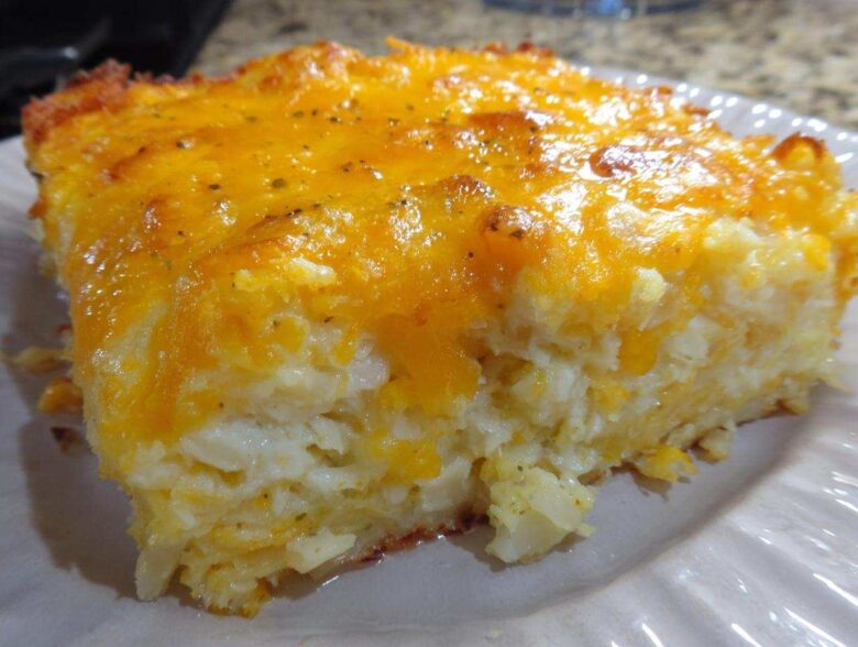Close-up of a square serving of cheesy potato casserole topped with melted, golden cheddar cheese.