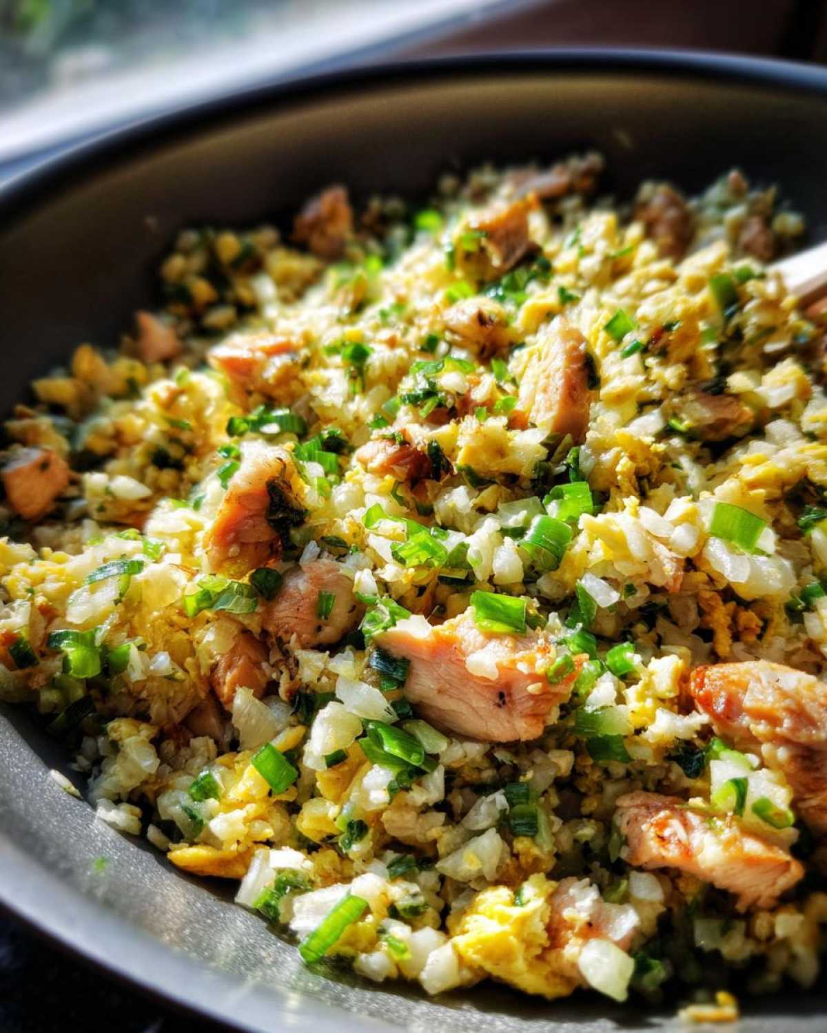 Close-up of savory chicken cauliflower fried rice, featuring scrambled egg, chopped green onions, and chunks of chicken.
