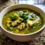 Close-up of a bowl of vibrant green chicken poblano soup recipe, topped with shredded chicken, avocado chunks, and fresh cilantro.