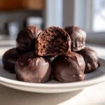 A stack of rich, chocolate-coated oreo balls, with one cut in half revealing the dark, cakey interior.