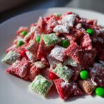 Close-up of vibrant red and green Christmas puppy chow coated in powdered sugar, mixed with colorful candies.