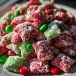 Close-up of vibrant red and green Christmas puppy chow coated in powdered sugar, mixed with red and green candies.