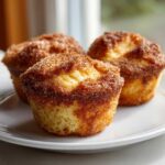Three golden french toast muffins topped generously with sparkling cinnamon sugar, served on a white plate.