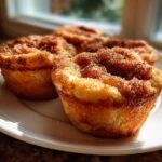 Three golden brown french toast muffins topped with a thick layer of cinnamon sugar on a white plate.
