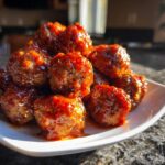 A close-up of a pile of glazed cranberry meatballs served on a white dish.