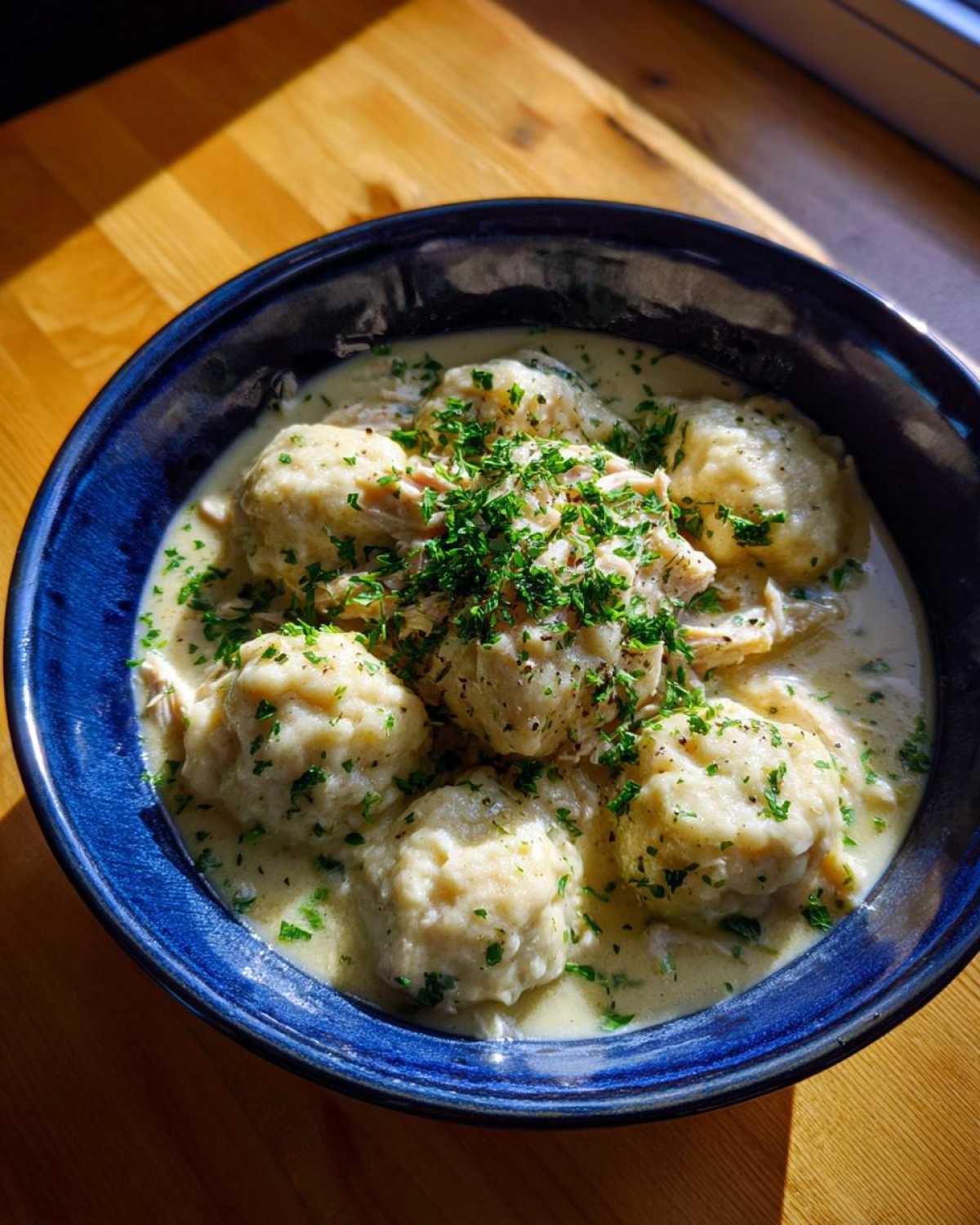 A deep blue bowl filled with creamy chicken and dumpling, topped generously with fresh chopped parsley.