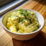 A white bowl filled with creamy, yellow egg salad recipe, garnished generously with fresh dill.