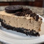 A generous slice of creamy peanut butter pie with a dark chocolate crust, topped with cookie crumbs and a whole Oreo.