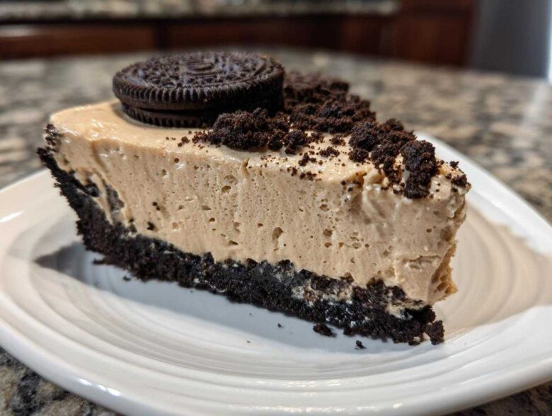 A generous slice of creamy peanut butter pie with a dark chocolate crust, topped with cookie crumbs and a whole Oreo.