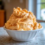 A large mound of creamy, orange pumpkin fluff, sprinkled with cinnamon, served in a white bowl.