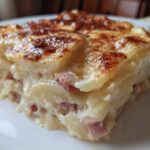 A close-up of a creamy slice of scalloped potatoes and ham with a golden-brown, cheesy top.