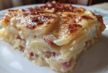 A close-up of a creamy slice of scalloped potatoes and ham with a golden-brown, cheesy top.