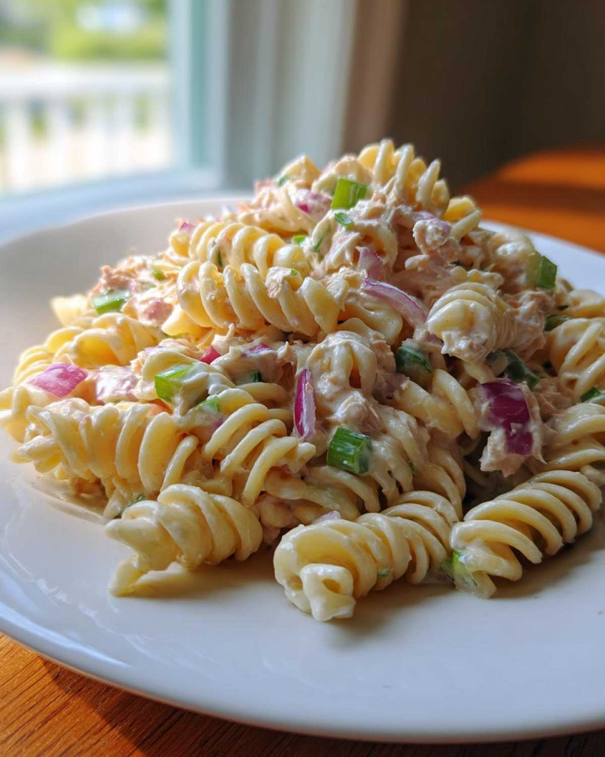 A serving of creamy tuna pasta salad made with rotini pasta, red onion, and green onion on a white plate.