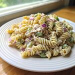 A close-up of creamy tuna pasta salad made with rotini pasta, celery, and red onion on a white plate.