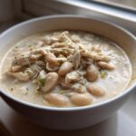 Close-up of a bowl of creamy white chicken chili with shredded chicken and white beans.