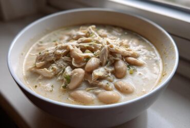 Close-up of a bowl of creamy white chicken chili with shredded chicken and white beans.