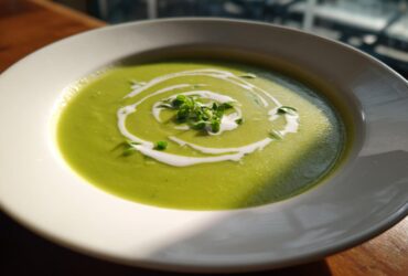 A vibrant bowl of creamy green zucchini soup, garnished with a white cream swirl and fresh microgreens.