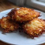 Three golden-brown, crispy potato latkes piled on a white plate, showcasing their shredded texture.