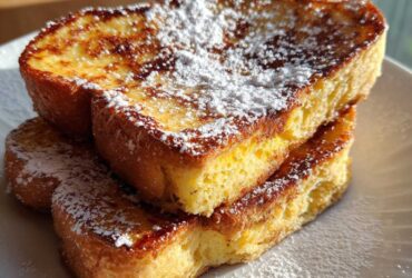 A stack of three slices of golden brown easy french toast dusted generously with powdered sugar on a white plate.