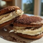 Two decadent tiramisu cookies, featuring dark chocolate wafers and thick cream filling, dusted with cocoa powder.