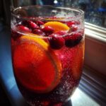 Close-up of a fizzy, red Thanksgiving punch garnished with fresh cranberries and bright orange slices.
