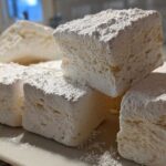 Close-up of large, fluffy homemade marshmallows dusted heavily with powdered sugar.