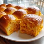 Close-up of fluffy, golden-brown sweet potato rolls, one split open revealing the soft orange interior.