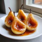 Four beautifully caramelized baked pears glistening with syrup, served on a white plate.
