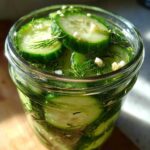 Close-up of fresh cucumber slices and dill being prepared for refrigerator pickles in a glass jar.