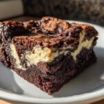 A close-up of a rich, fudgy cream cheese brownies slice showing the dark chocolate base and creamy white swirl.